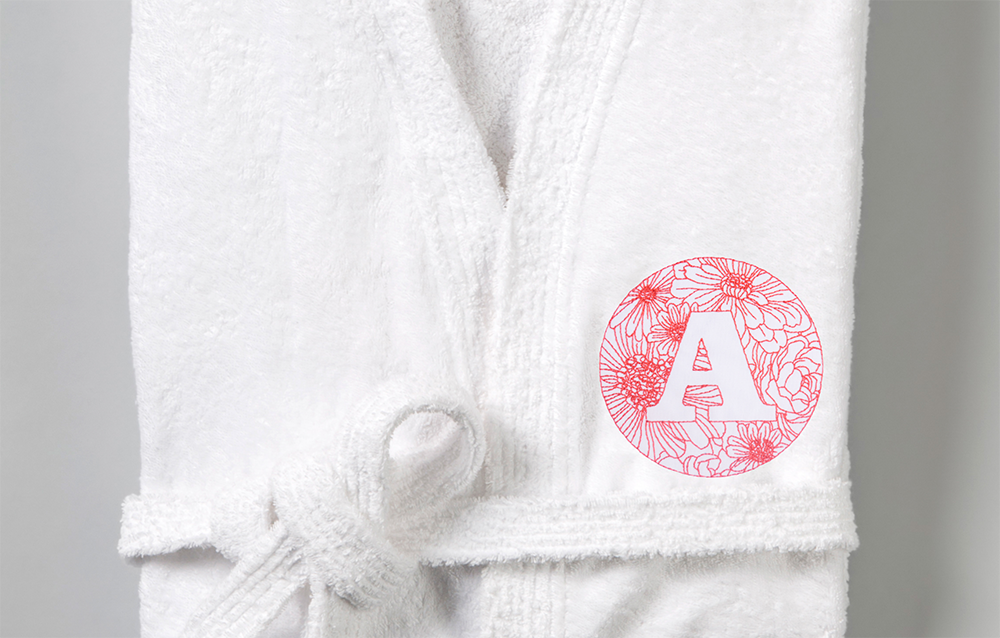 Folded white bath gown adorned with an intricately embroidered decorative letter 'A' monogram.